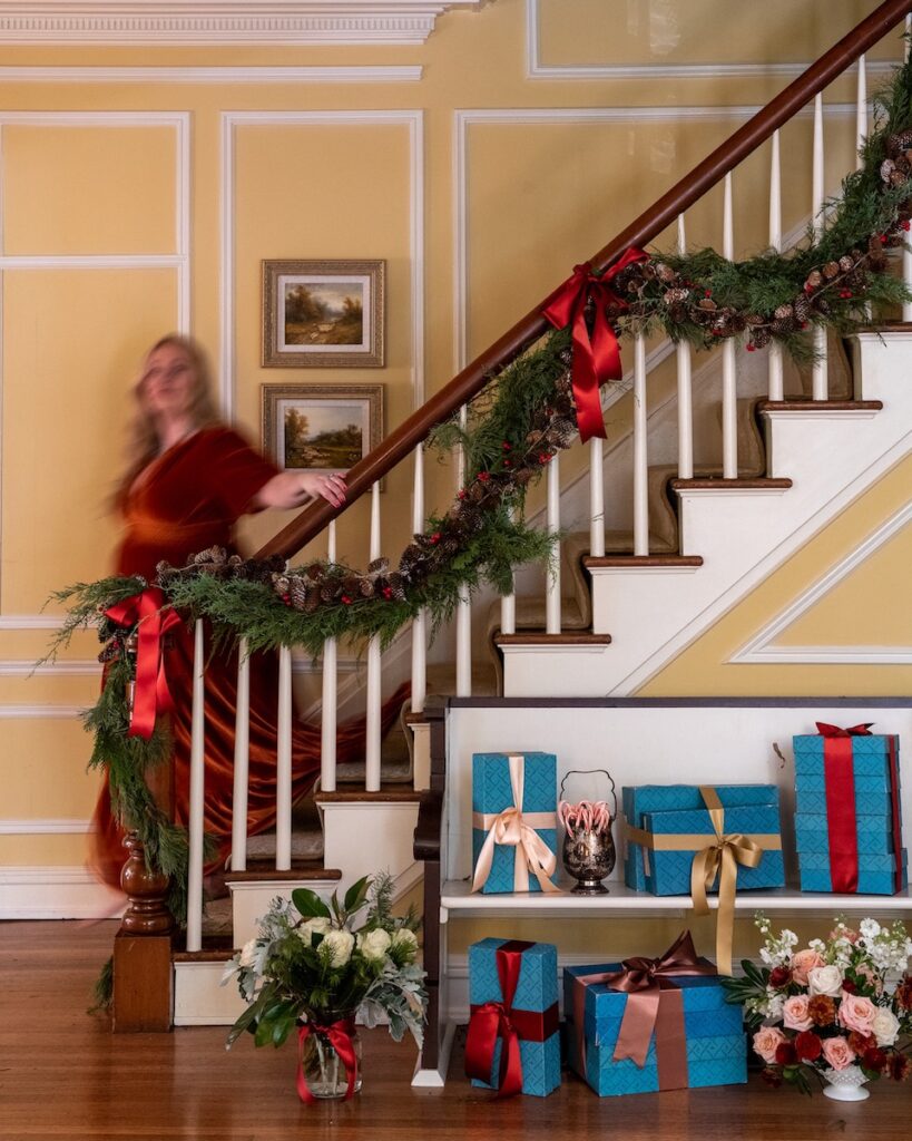 A photo with a slight motion blur of Gwen Martin, on the stairwell of her Sewickley home decorated with Christmas decorations