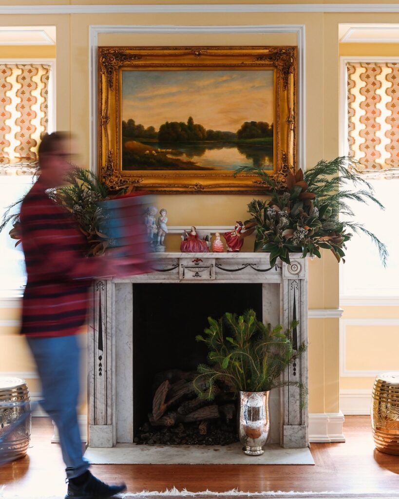 A figure with a motion blur walks past Gwen Martin's mantlepiece with a large framed landscape painting above it