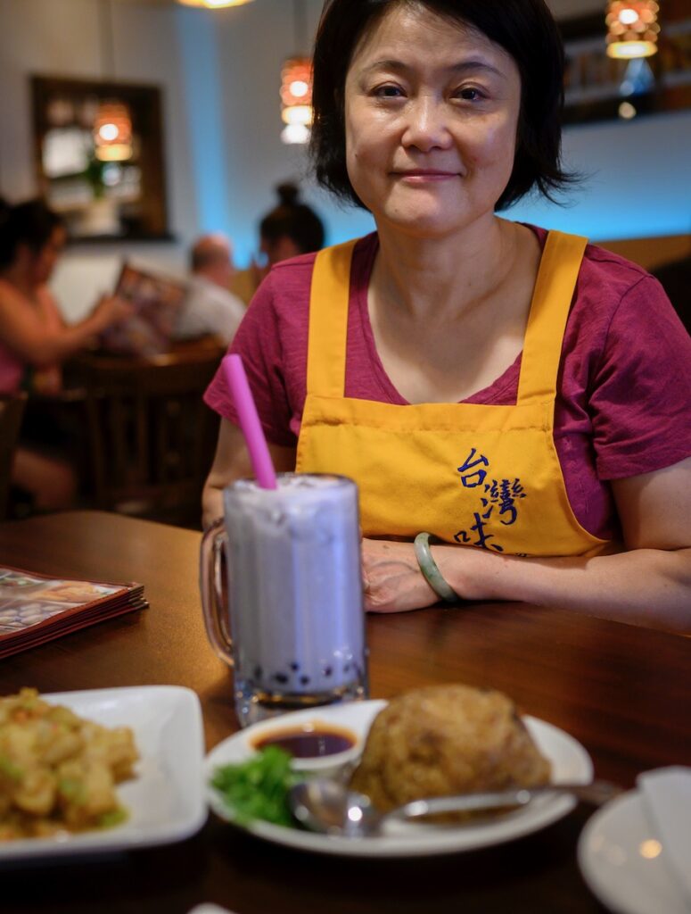 Jenny Tao beams at the camera from in front of a table of bubble tea and snacks