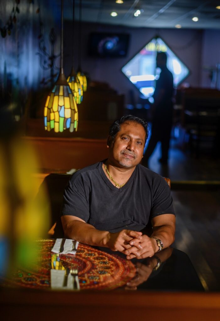 The owner of Coriander sits at a table in his restaurant, smiling 