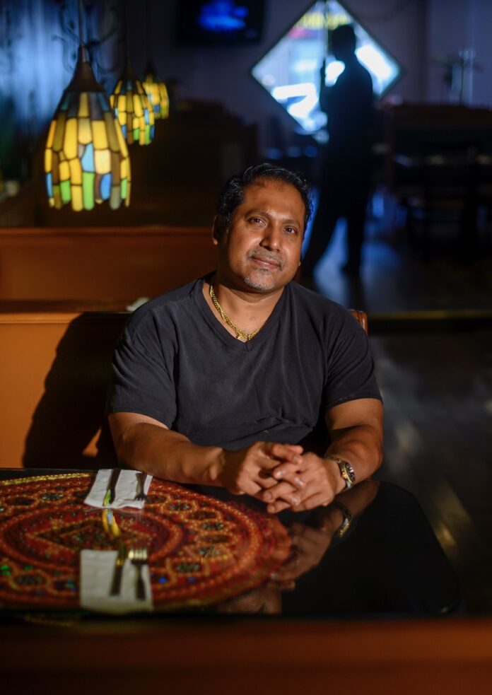 A man sits at a diner table in Coriander, a Pittsburgh restaurant, smiling at the camera