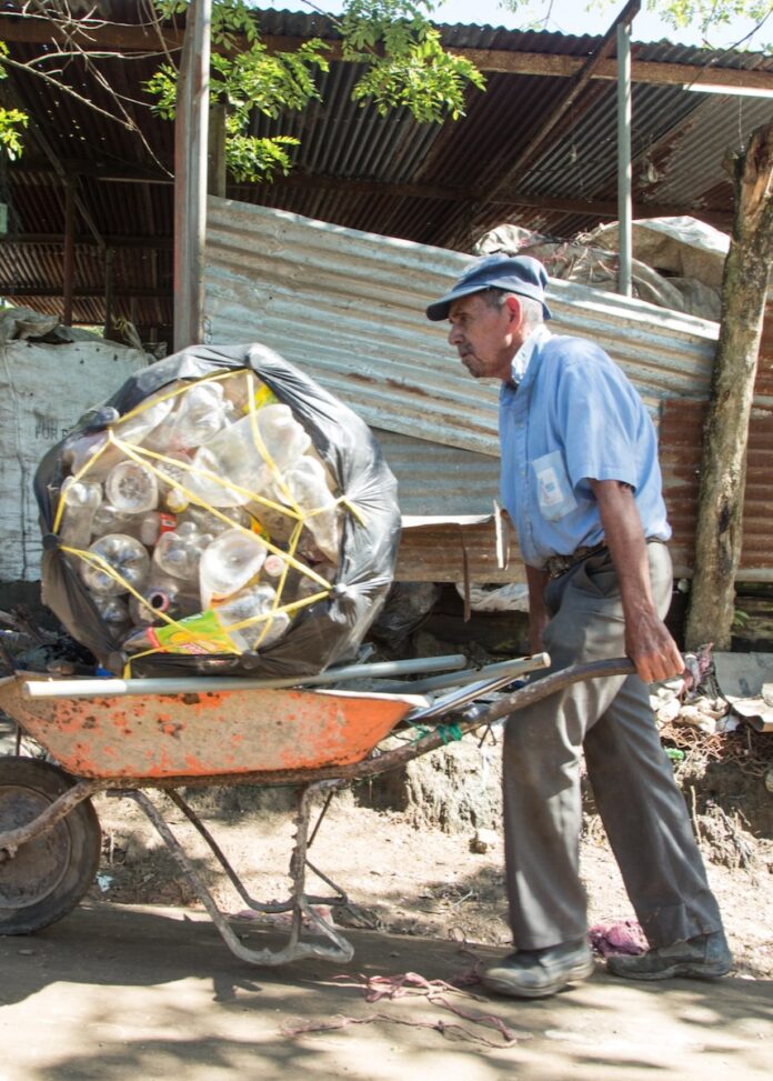 An older man pushing a wheelbarrow of trash.