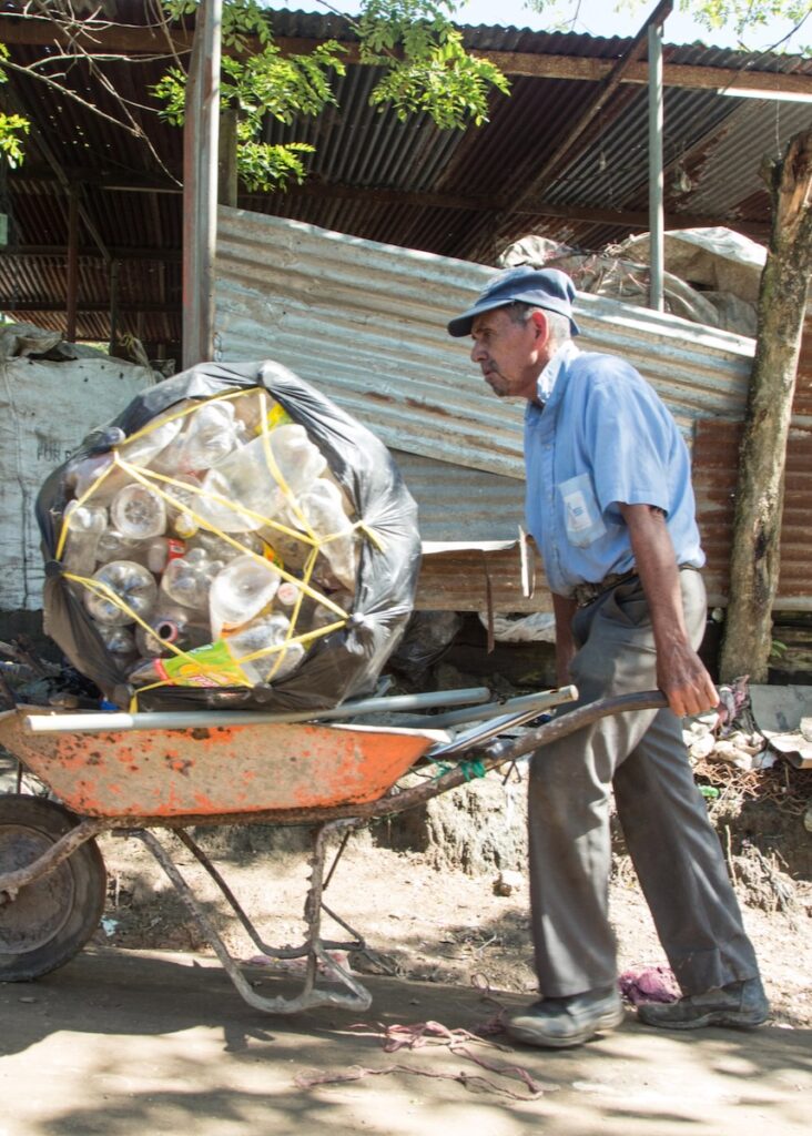 An older man pushing a wheelbarrow of trash.