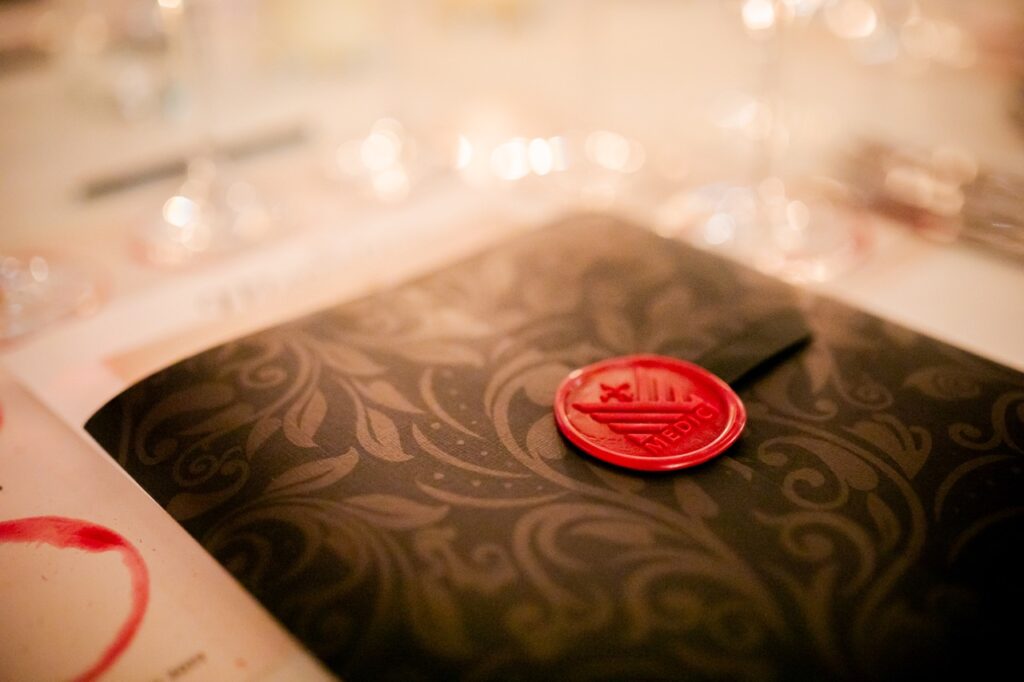 A black envelop sits on a table with a red seal on it that says Medici.