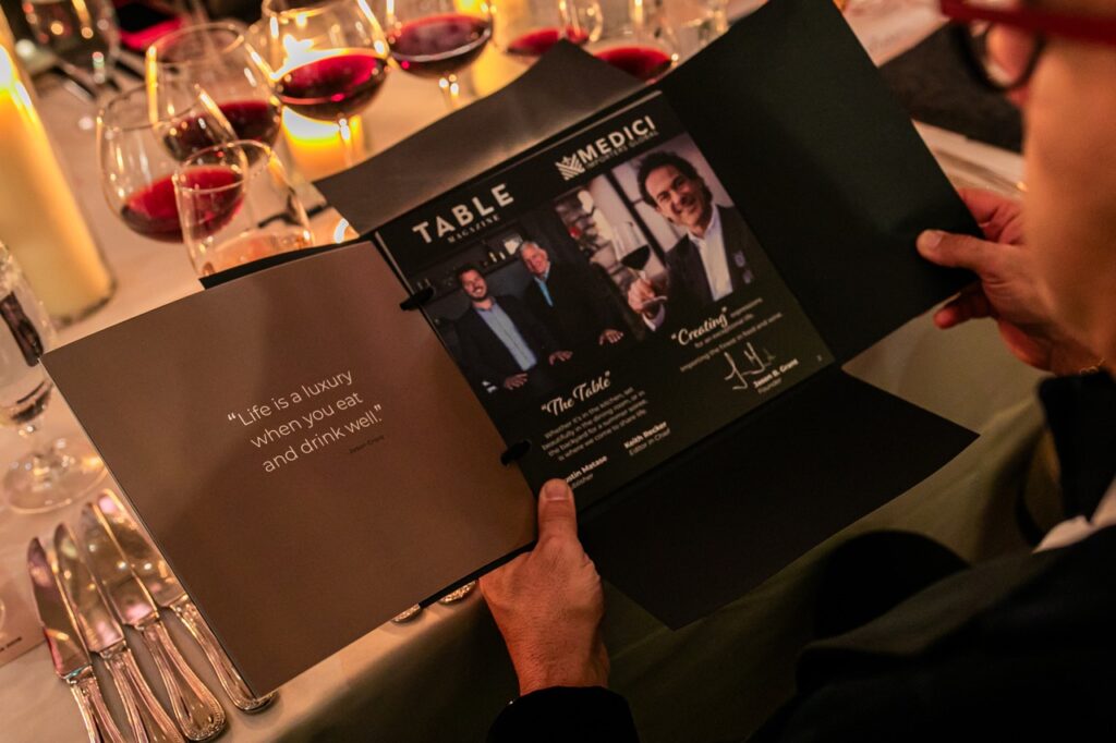A man looks at a folder which displays TABLE Magazine and Medici staff.
