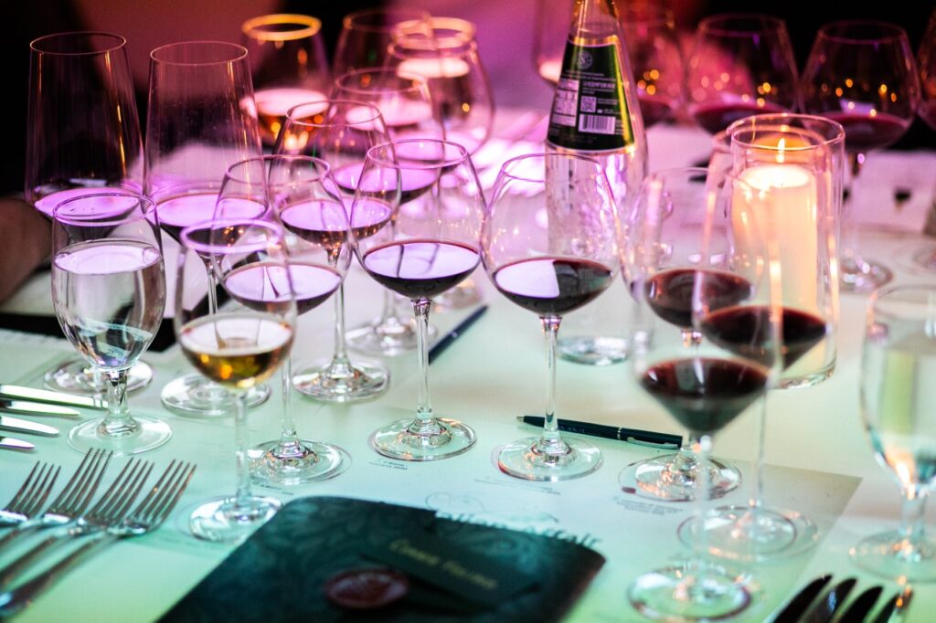 A variety of barely filled wine glasses sit on a pale green table with purple lights coming down in the back.