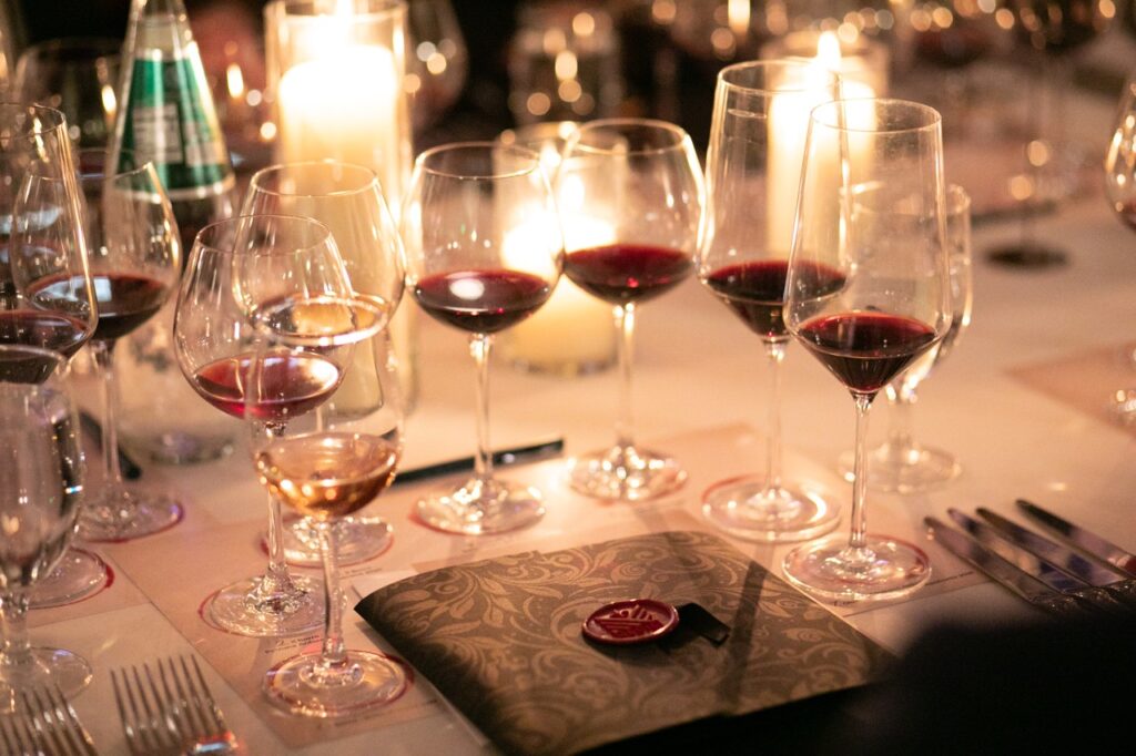 A variety of partially filled wine glasses sit on a candlelit table around a folder with a red seal.