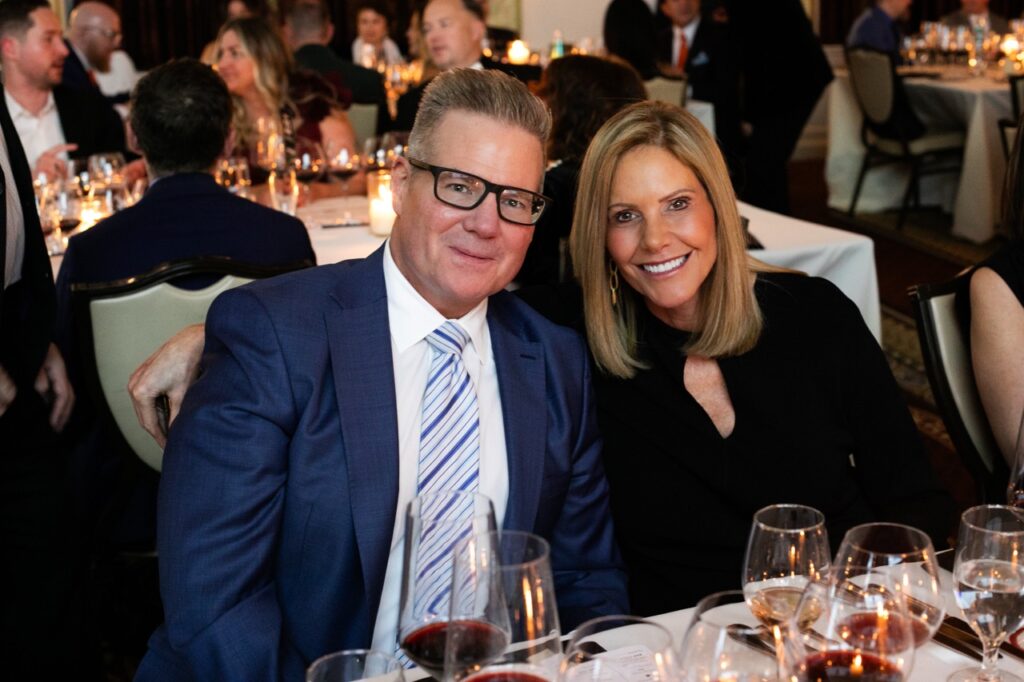 A man in a blue suit smiles with a woman in a black dress.