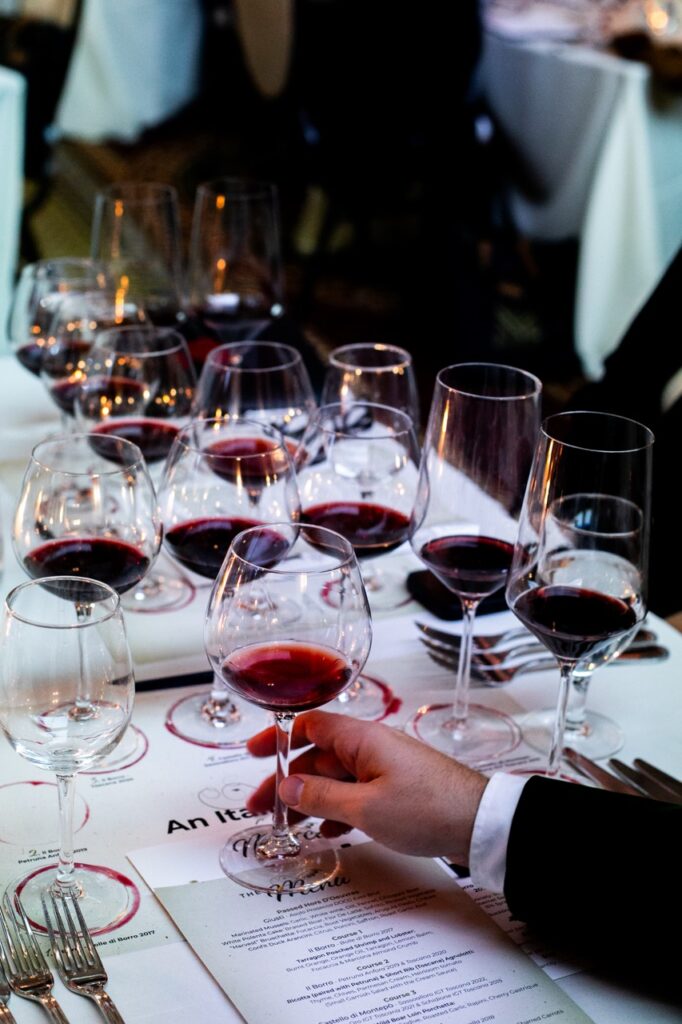 A person holds the stem of a wine glass on a table amongst other glasses of wine.