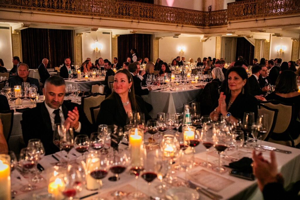 People sit at a candlelit table with wine glasses on them and clap their hands.