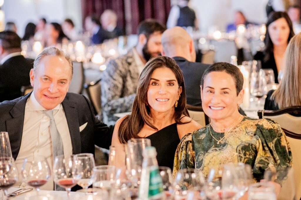 Two women and a man smile in warm candlelight at a table with wine glasses.