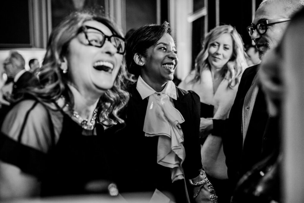 Two women laugh out loud with a man and another woman in the background, all in black and white.