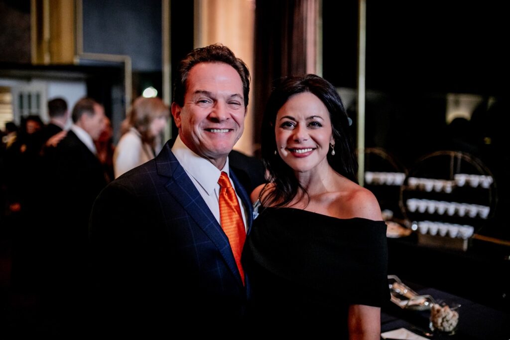 A man with an orange tie smiles with a woman in a black dress.
