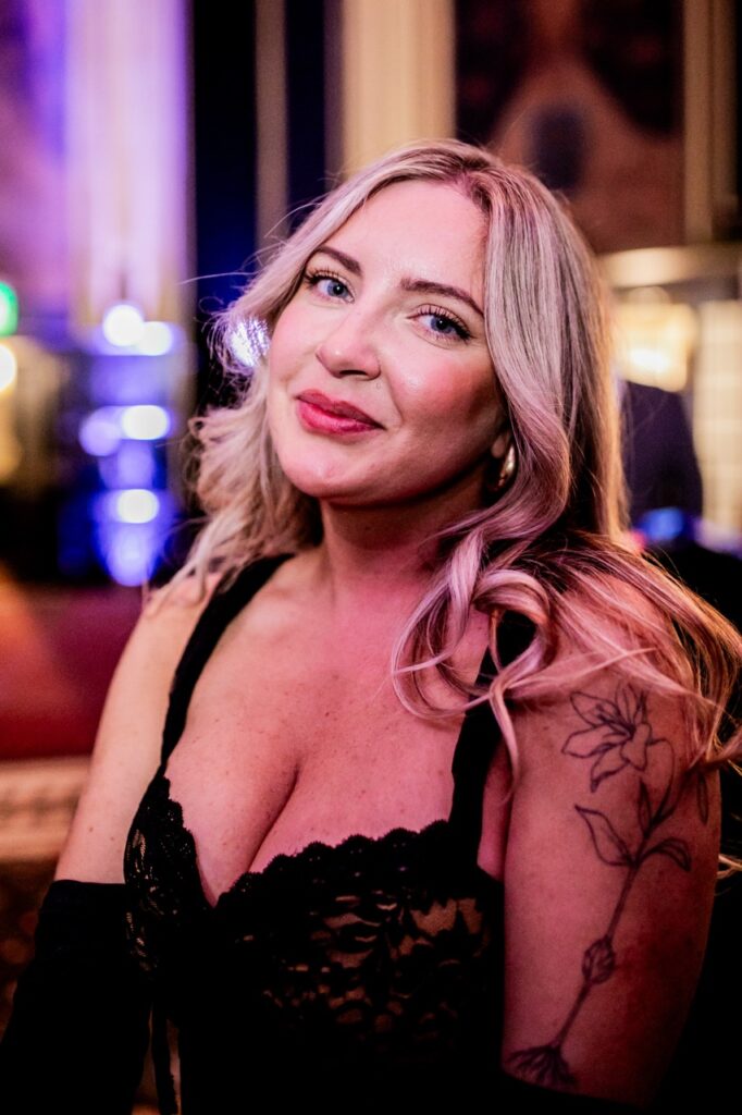 A woman with blonde hair and a black lace top smiles for the camera.