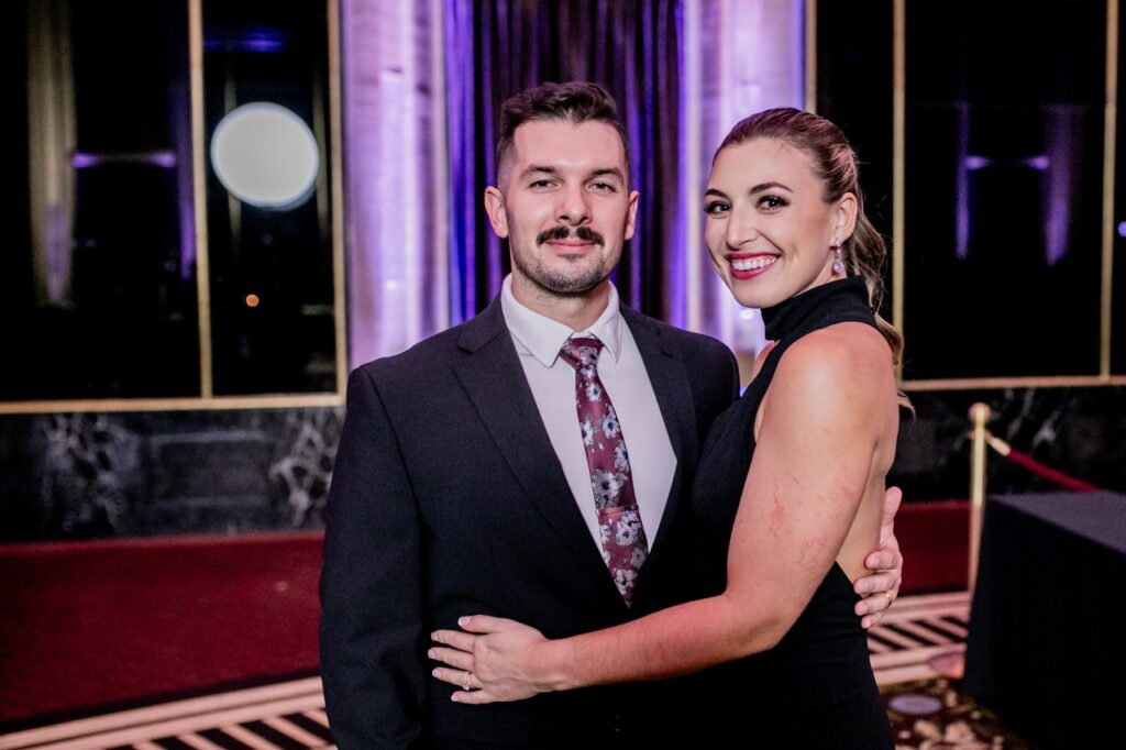 A man in a suit jacket has a woman in a black dress holding on to him.