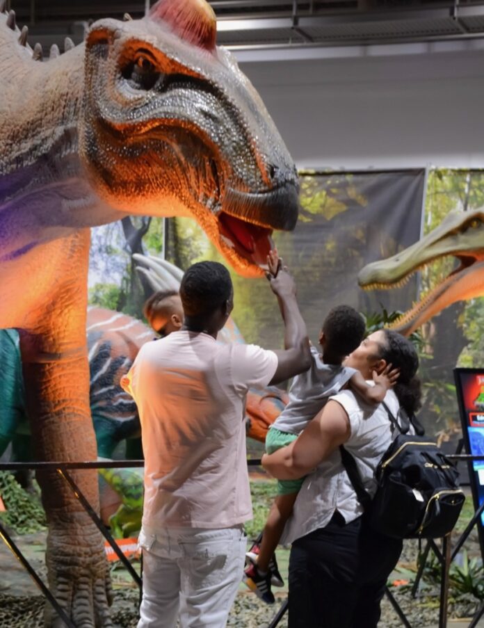 A family stands together reaching up to touch a life size dinosaur at an event in Pittsburgh.