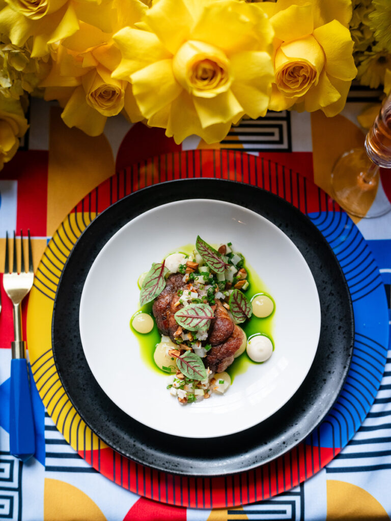 A colorful and artfully presented dish featuring tender meat, vibrant green sauce, and fresh herbs.