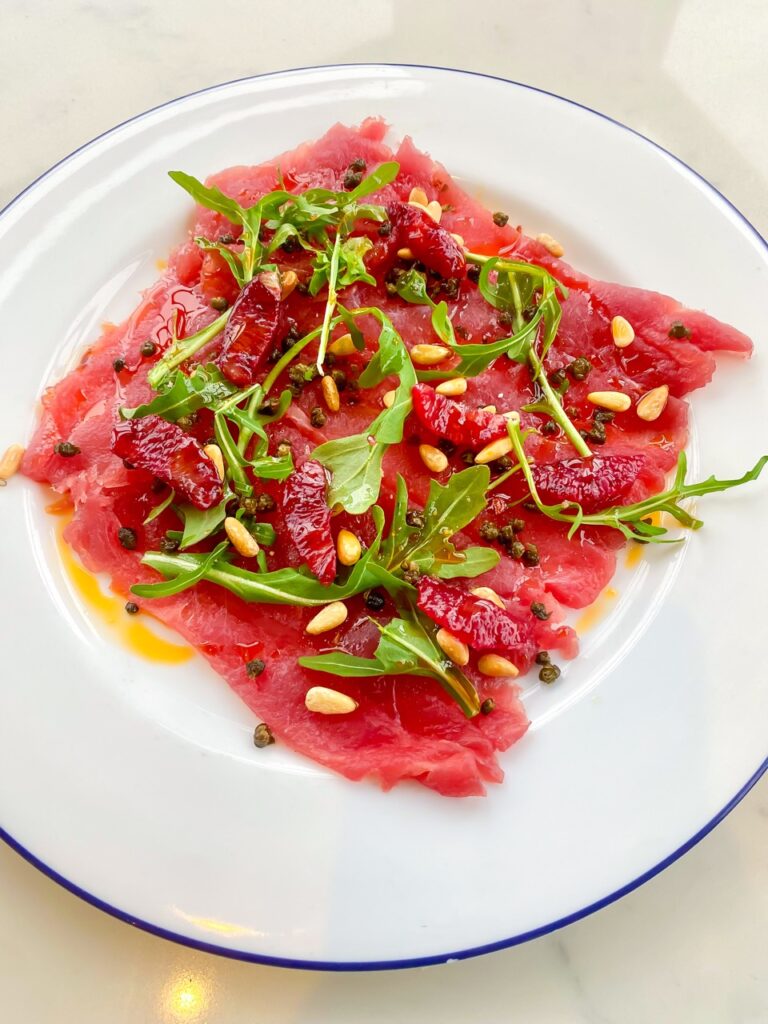 A white plate of ahi tuna with herbs.