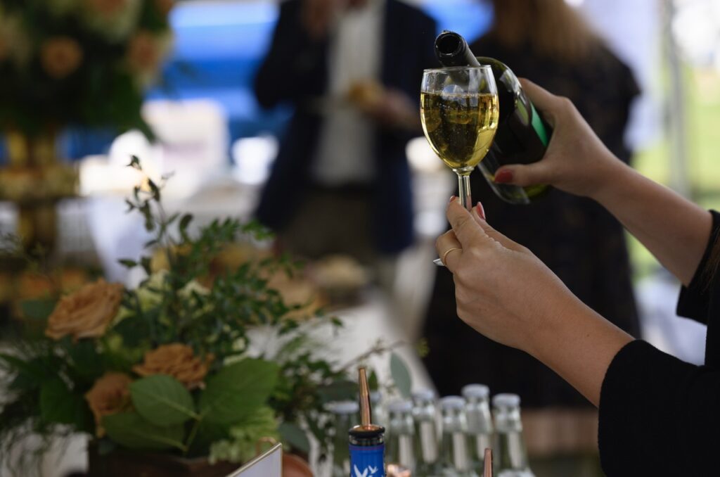 A woman pours a wine bottle into a wine glass.