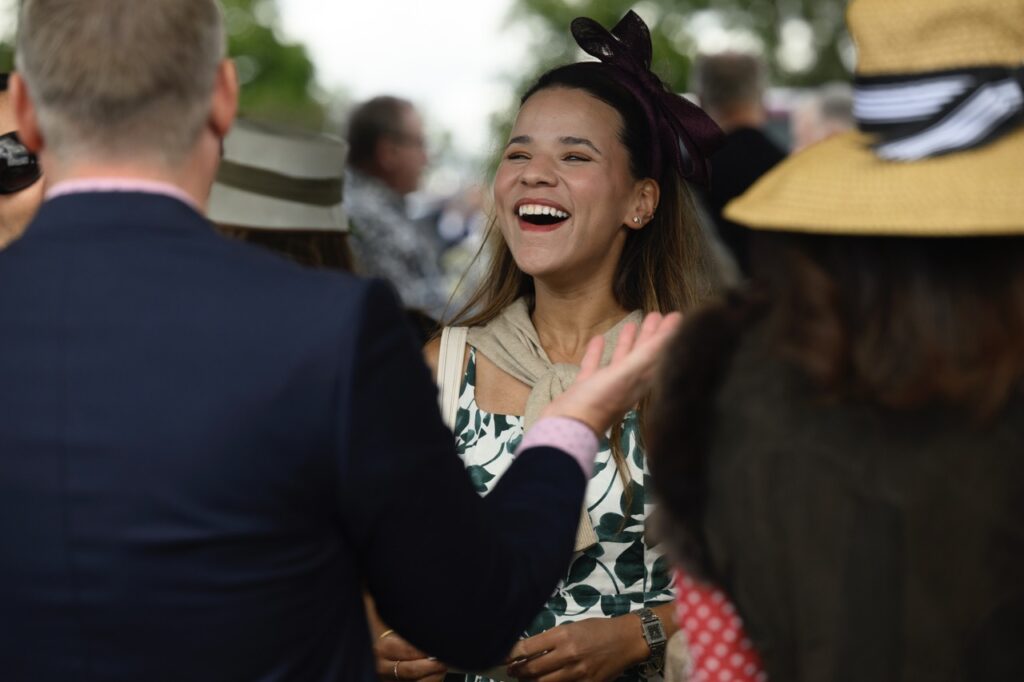 A woman with a big bow on her head and red lipstick laughs at a man in a blue sports coat.