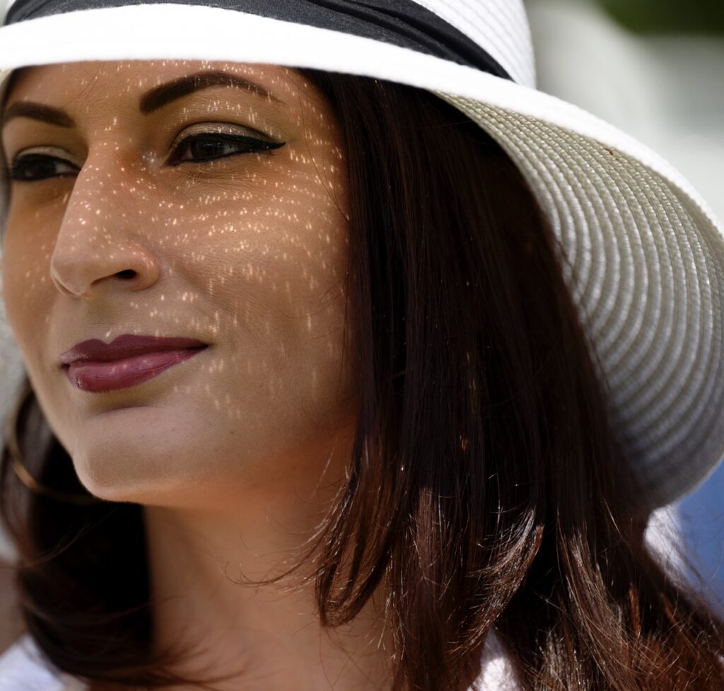 A woman in a white sun hat has light reflecting in a pattern on her face.