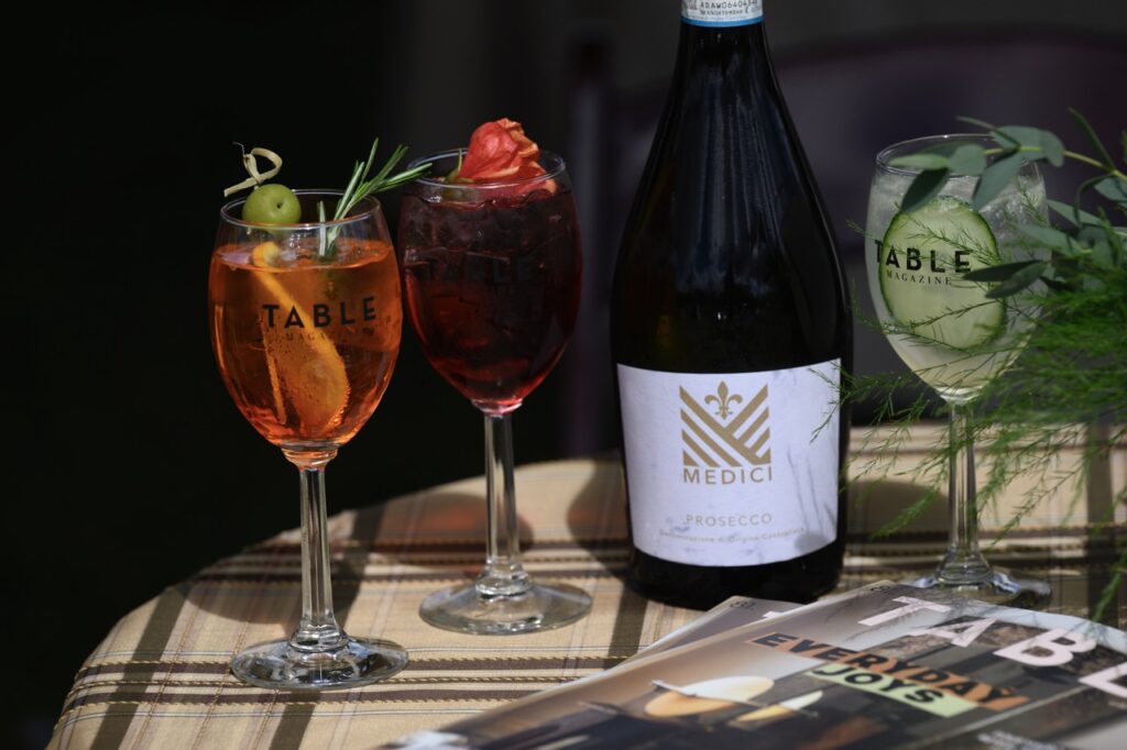 A table set up with a medici wine bottle, three full wine glasses, and an issue of TABLE Magazine.