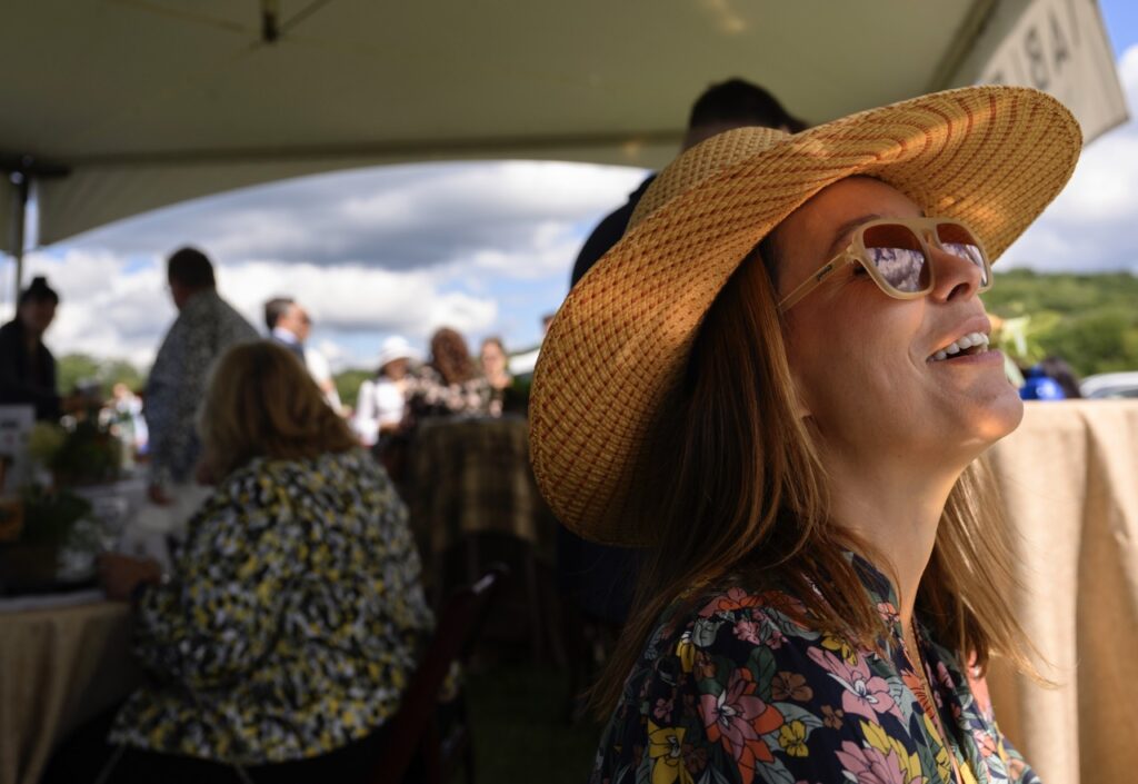 A woman in a brown sun hat and sunglasses looks up at the sky beyond the white tent.