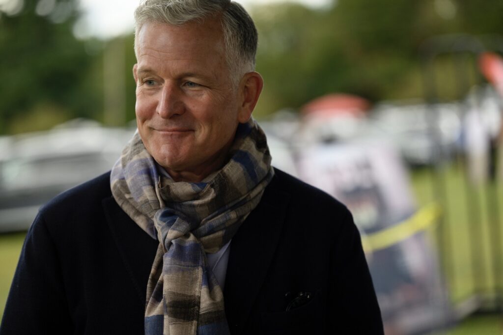 A man in a scarf and black sweater smiles at something off frame.