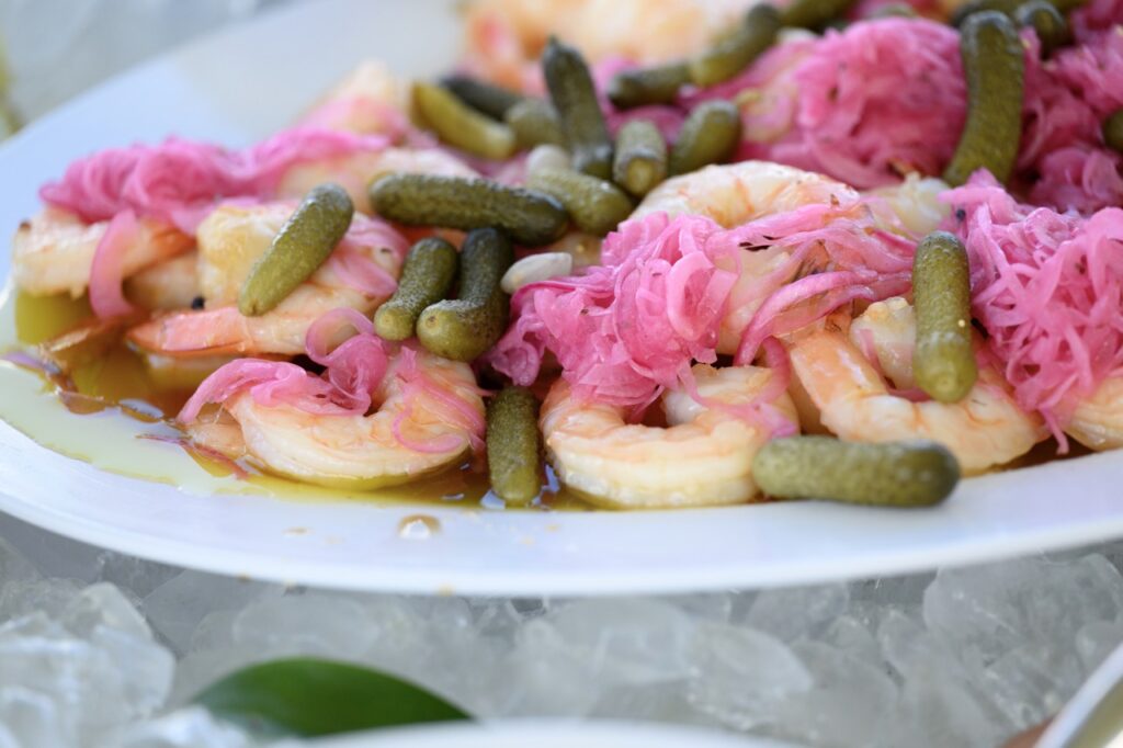 A white plate of shrimp with purple cabbage and mini pickles.