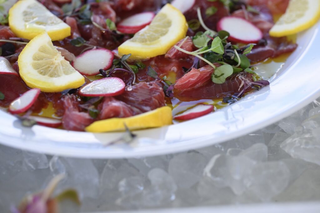 A white plate with raw salmon, lemon slices, beets, and greens.