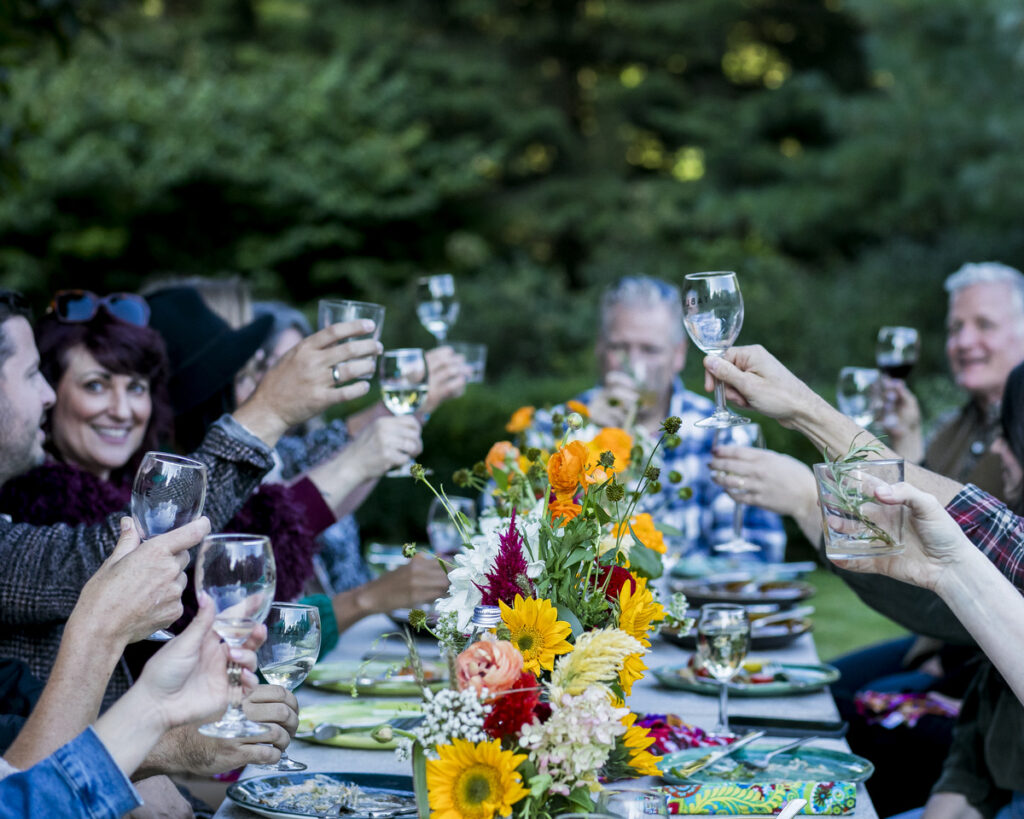 A group of people gathered around a long dining table in an outdoor setting, enjoying a festive gathering.