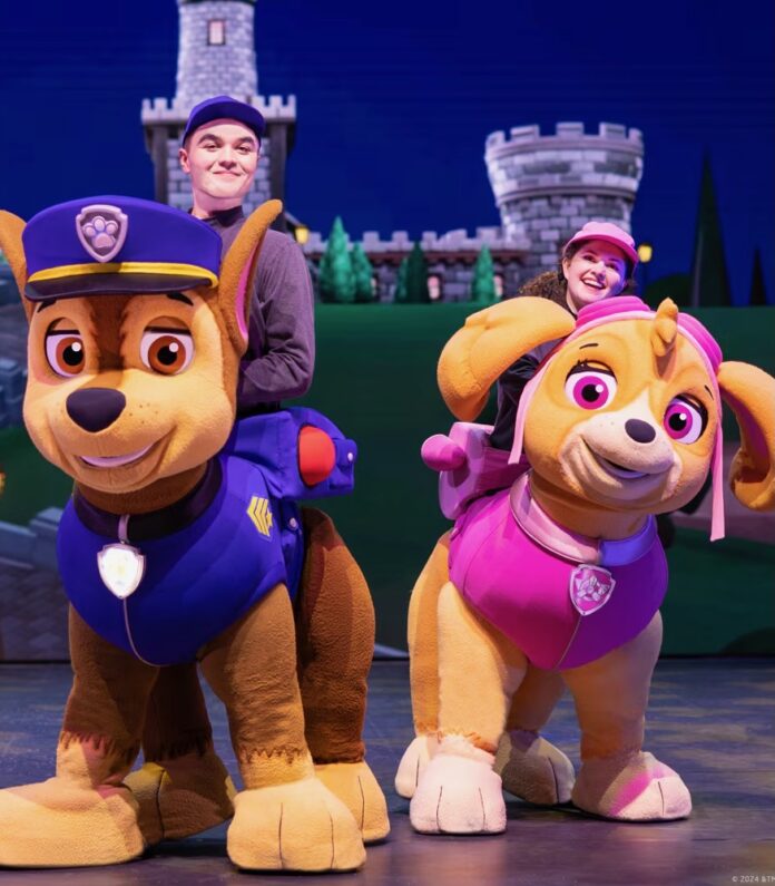 Two dog puppets controlled by two actors stand on a Pittsburgh stage, one in pink and one in blue.