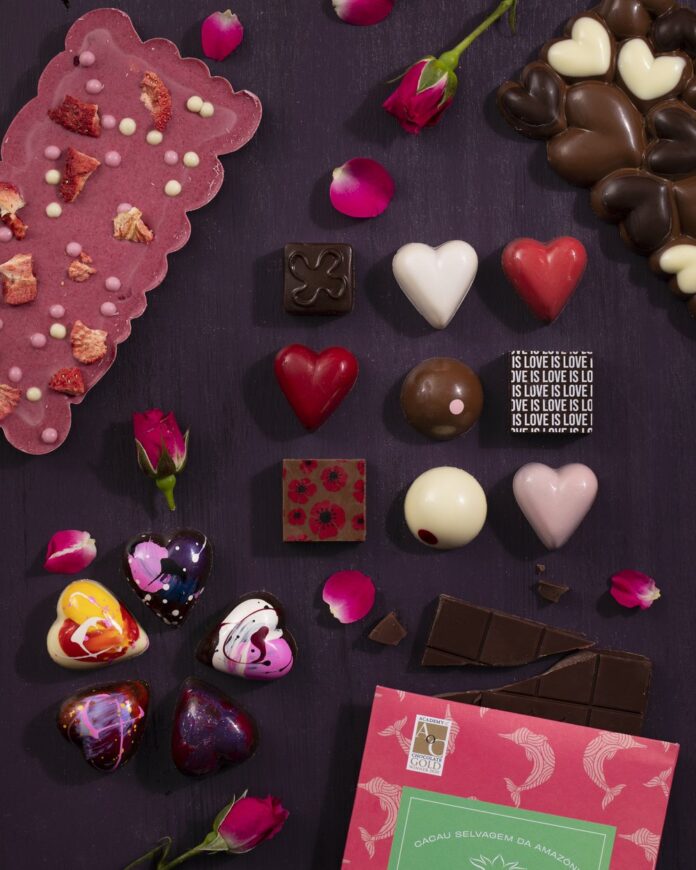 5 Pittsburgh Chocolate Shops for Valentine’s Day Candy Various chocolates in square, round, and heart shapes from Pittsburgh Chocolate shops sit on a purple background with boxes poking out of the corners.