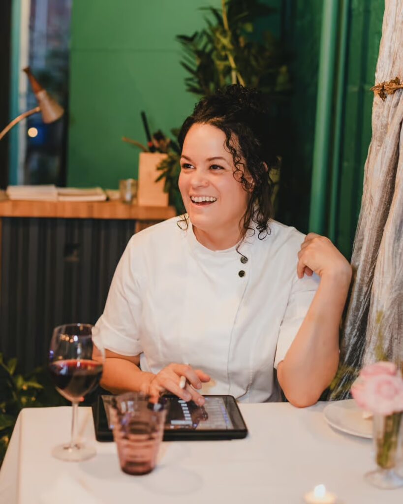 Chef Jamilka Borges sits at a table with a glass of wine in front of her.