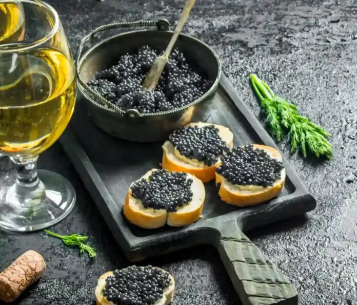 A plate of black caviar sits next to a glass of champagne on a black background, staged for a romantic meal