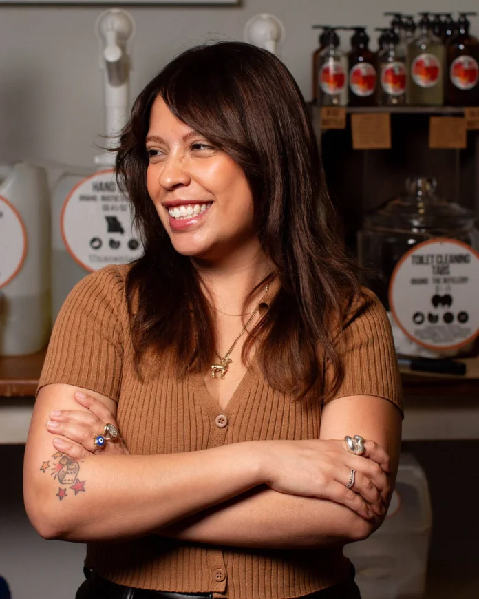 Larissa Russo stands with her arms crossed in front of her chest with bottles behind her from The Refillery in Pittsburgh.