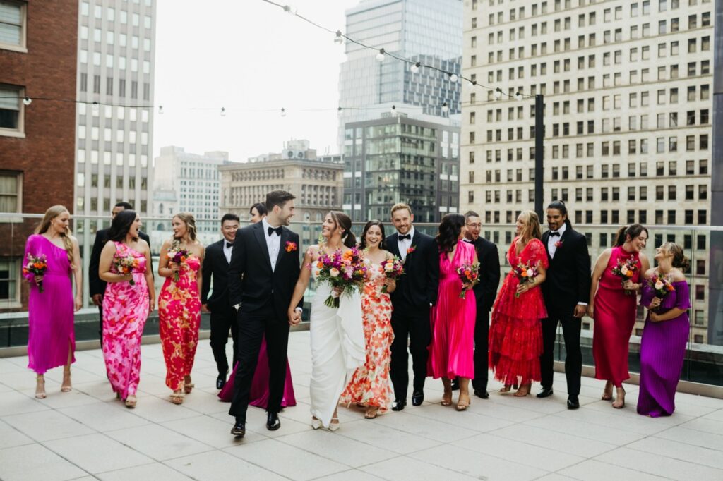 A group of colorful wedding guests stand behind a bride in a white dress and groom in a black suit.