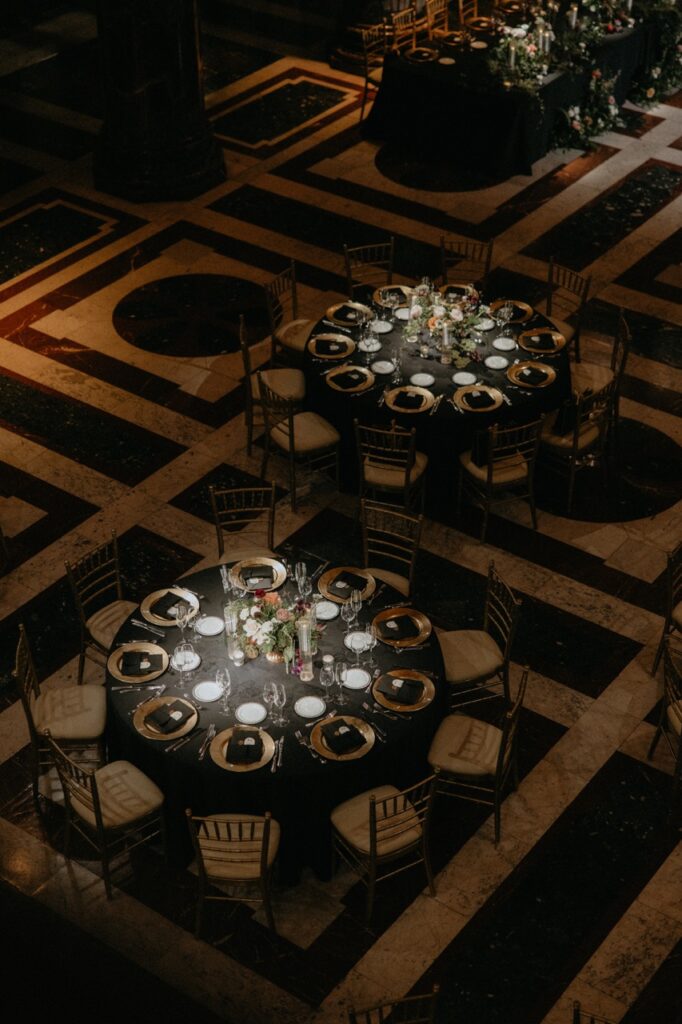 Two tables with plates, seats, and setting sit on a pattern floor under two spotlights.