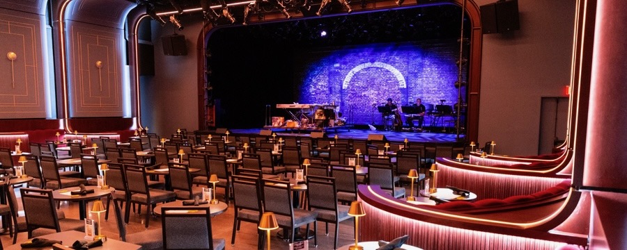 A stage and empty chairs in a music venue, with the stage lit in purple