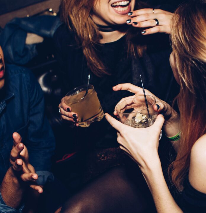 A woman laughs as she holds a glass with a group of friends at a late night hangout.