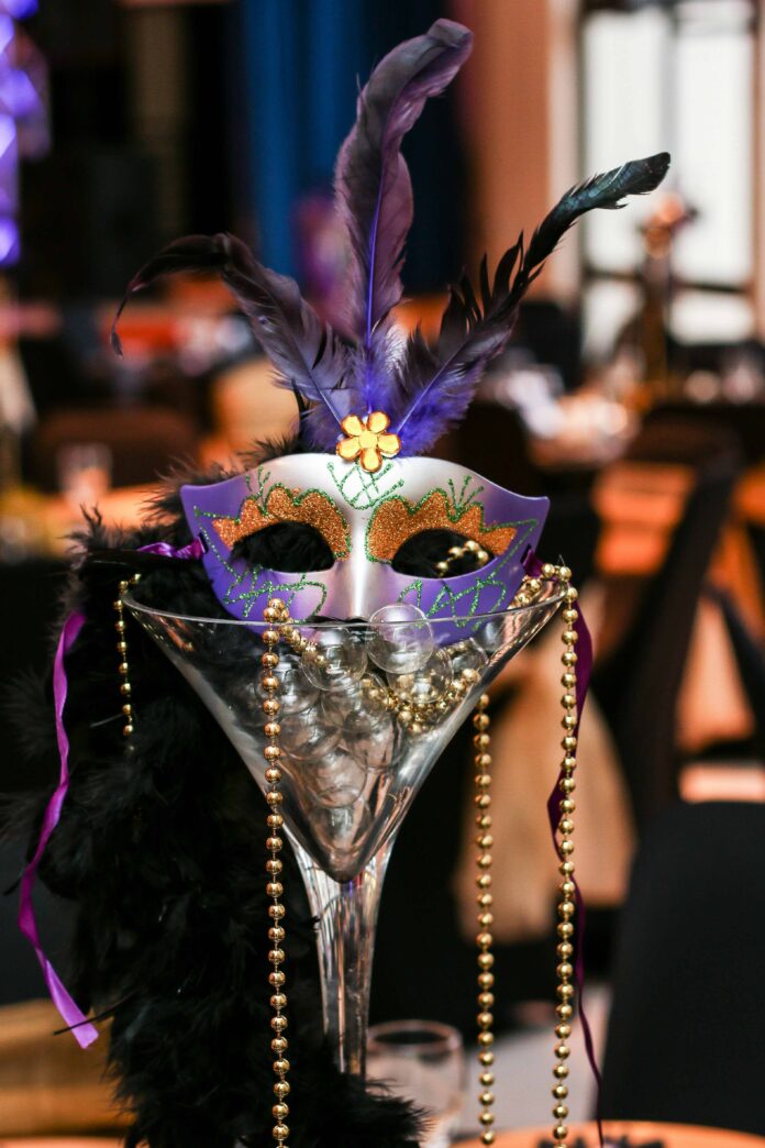 A Mardi Gras mask sits in a cocktail glass with bead necklaces hanging out of it.