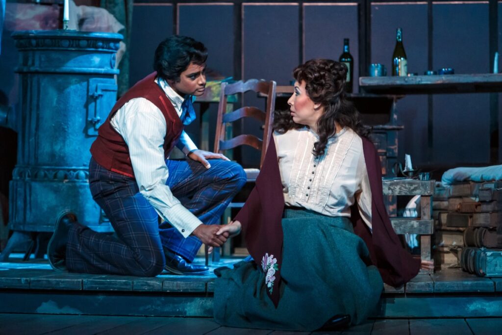 Two actors in La Boheme kneel at the front of a stage.