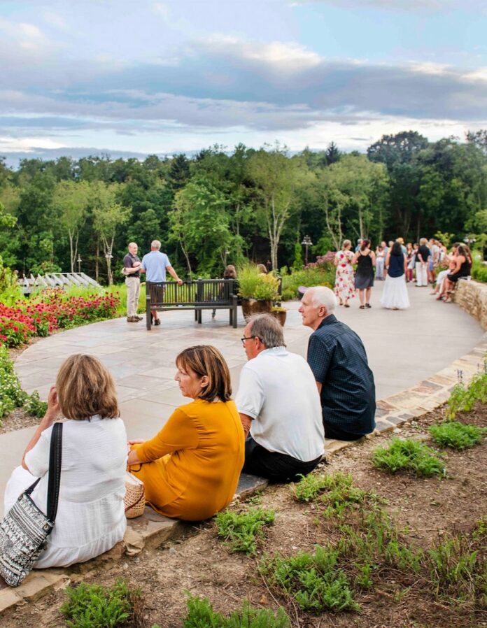A group of people walk around a concrete slab at the Pittsburgh Botanic Garden with trees and plants surrounding the area.