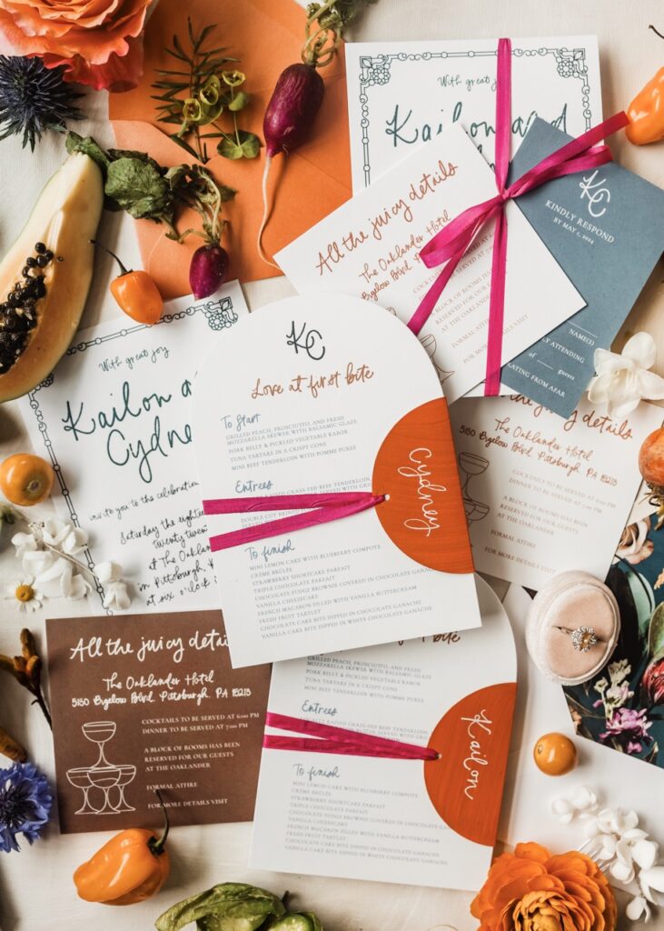 A variety of orange, white, pink, and brown wedding invitations sit on a table.