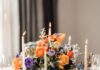 Wedding Rental Resources in Pittsburgh for Stylish Event Décor A table sits covered in white candles, orange and purple flowers, clear glasses, and white empty plates.
