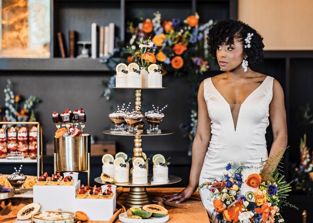 A bride in a white wedding gown admires a tiered assortment of desserts from a Pittsburgh baker.