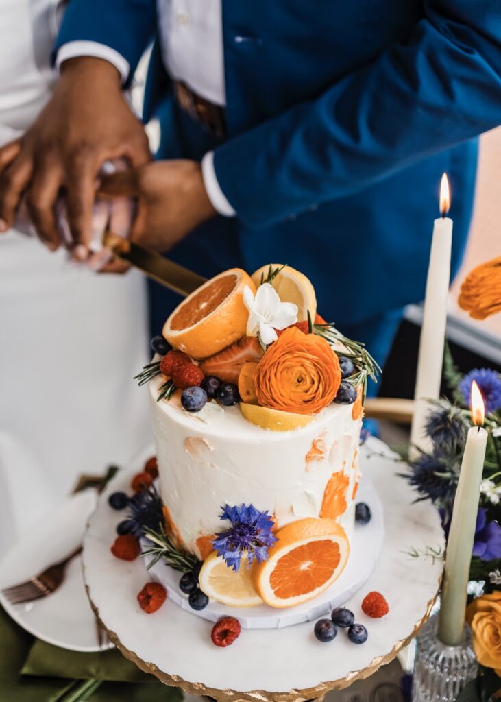 bride and groom cut their wedding cake that's white and covered in orange slices.