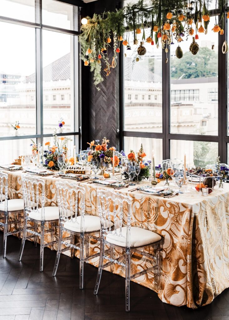 A wedding table decorated by a Pittsburgh service sits in the middle of a group of windows with flowers and orange candles adorning the table.