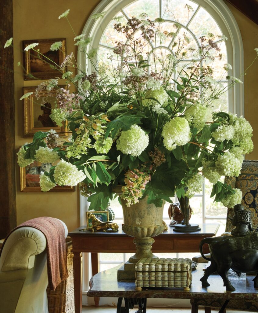 An interior design by Bunny Williams with white and green flowers in a gold vase.