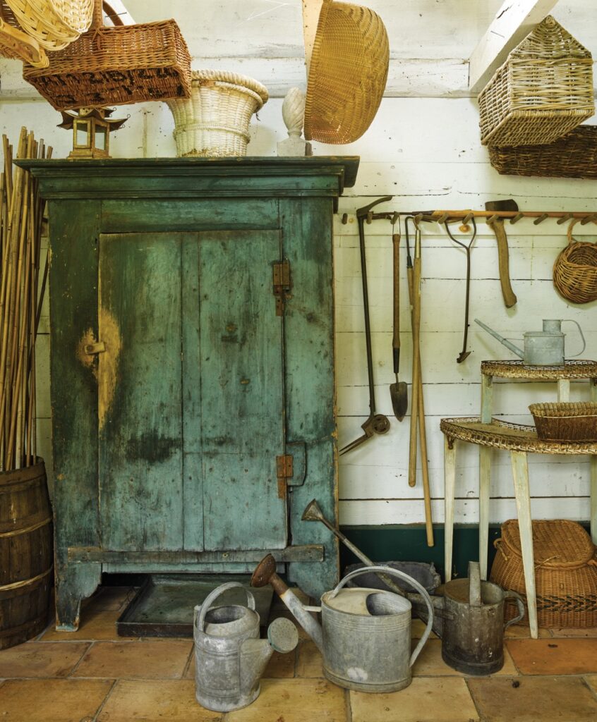 A green vintage cabinet with old farm tools sitting around it.